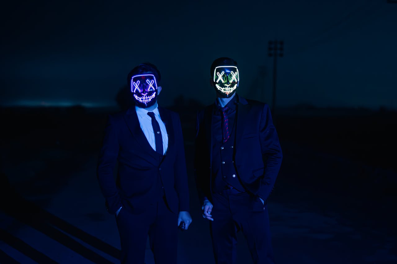 Two individuals in suits wearing illuminated LED masks under a dark night sky.